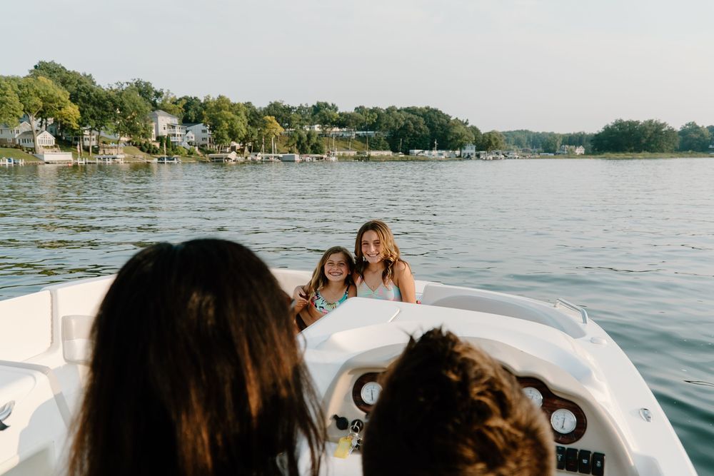 Group enjoys a sunny day boating on a scenic lake surrounded by green shoreline and boats in the distance.