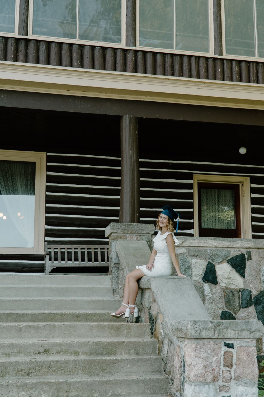 A person in white sits on stone steps of a rustic building with glass windows.