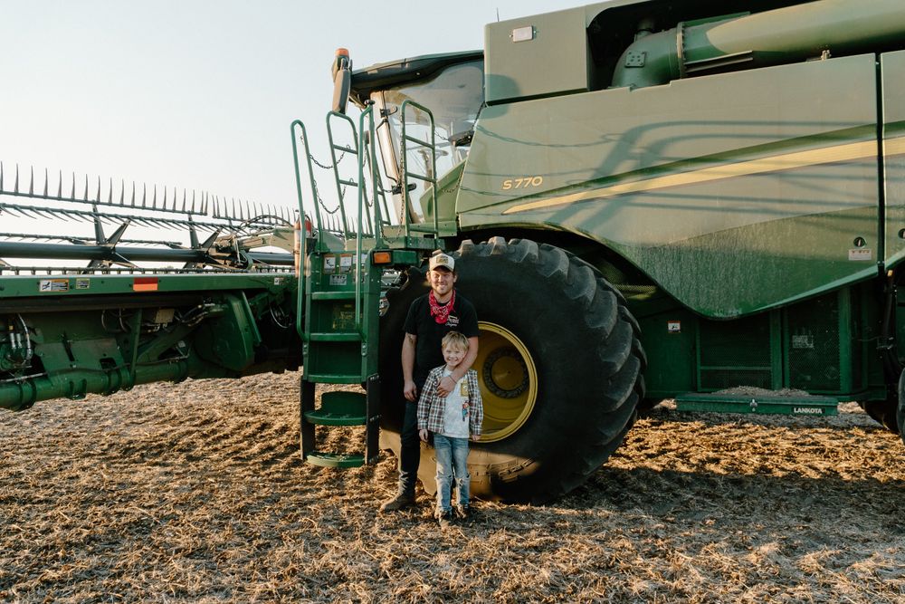 Large green John Deere combine harvester parked in a farm field at harvest time.