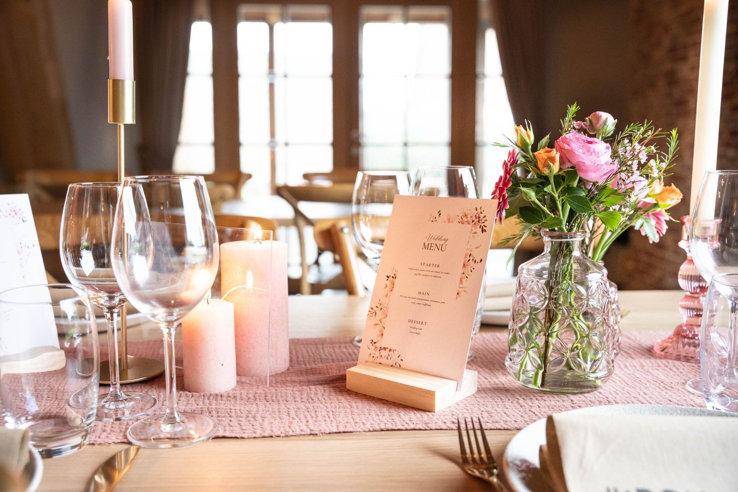 Elegant table setting with pink runner, menu cards and fresh floral arrangements in glass vases.