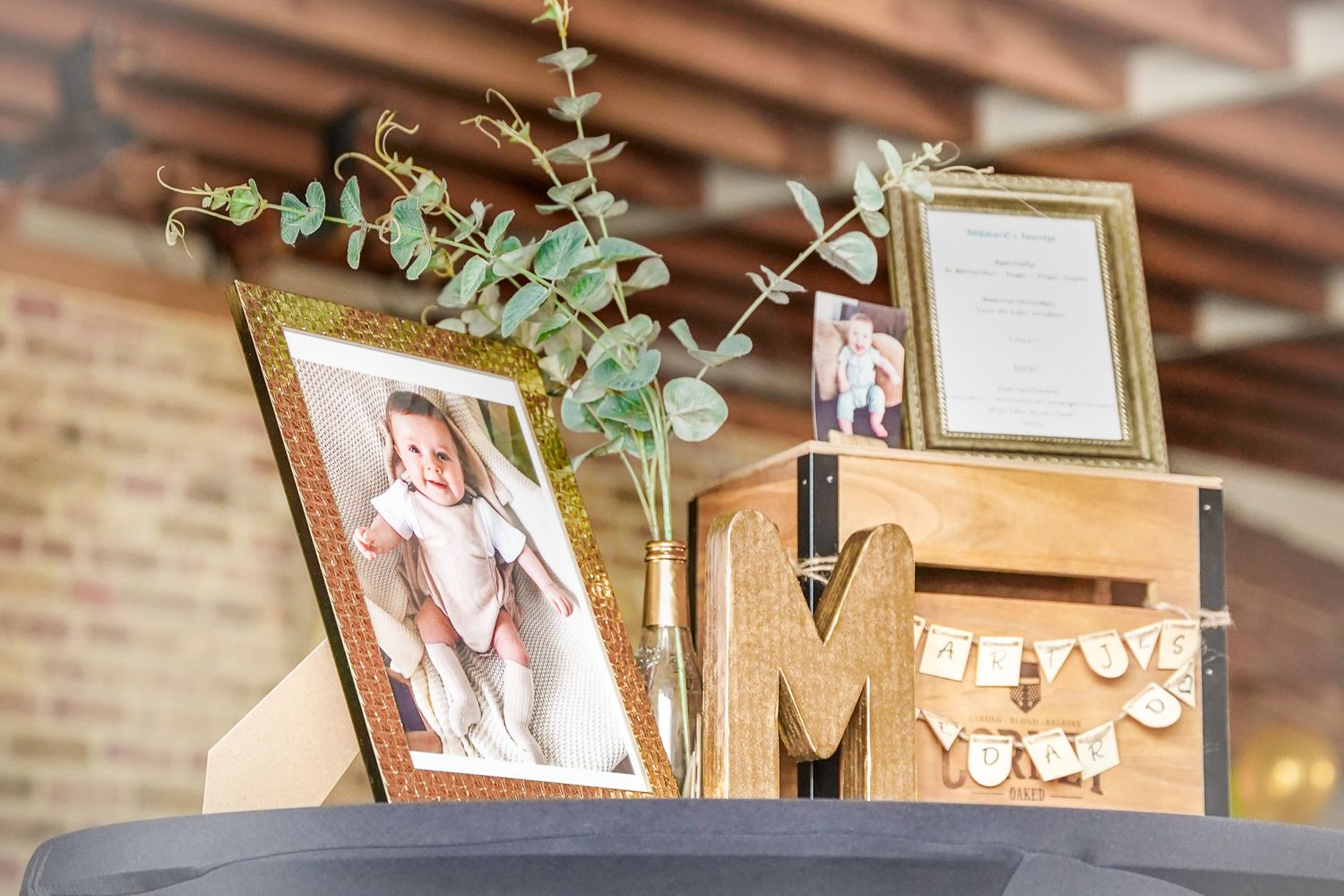 Decorative display with photo frames, eucalyptus branches, and wooden letter M on a table.