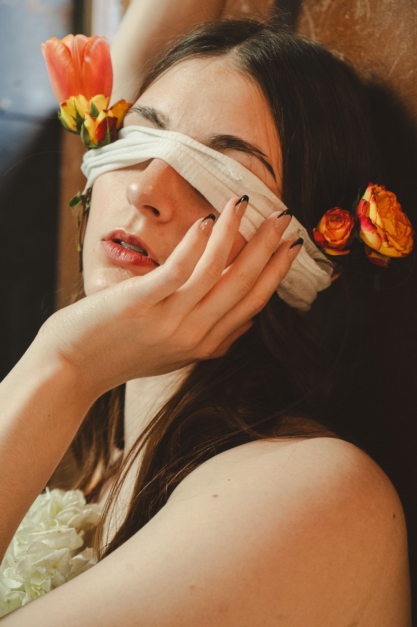 Artistic portrait with orange tulips and white blindfold in warm sunlight.