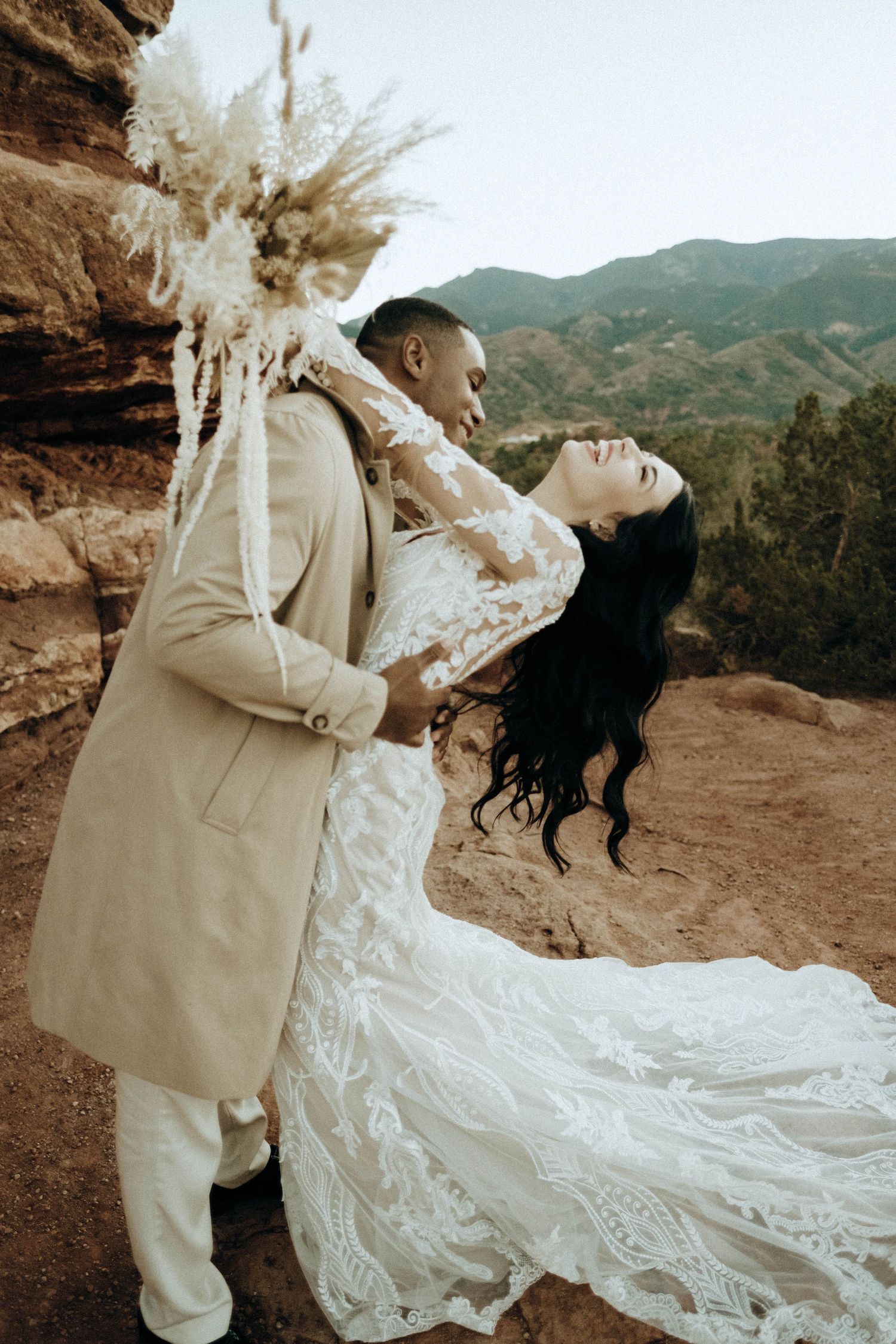 Groom dips bride in white lace dress at red rock outdoor wedding ceremony.