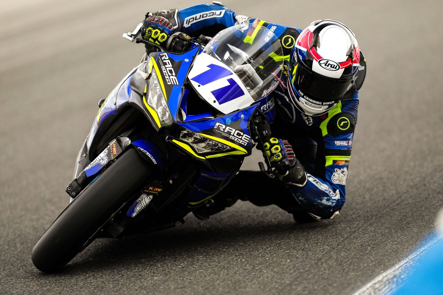A blue racing motorcycle leaning into a curve during competition.