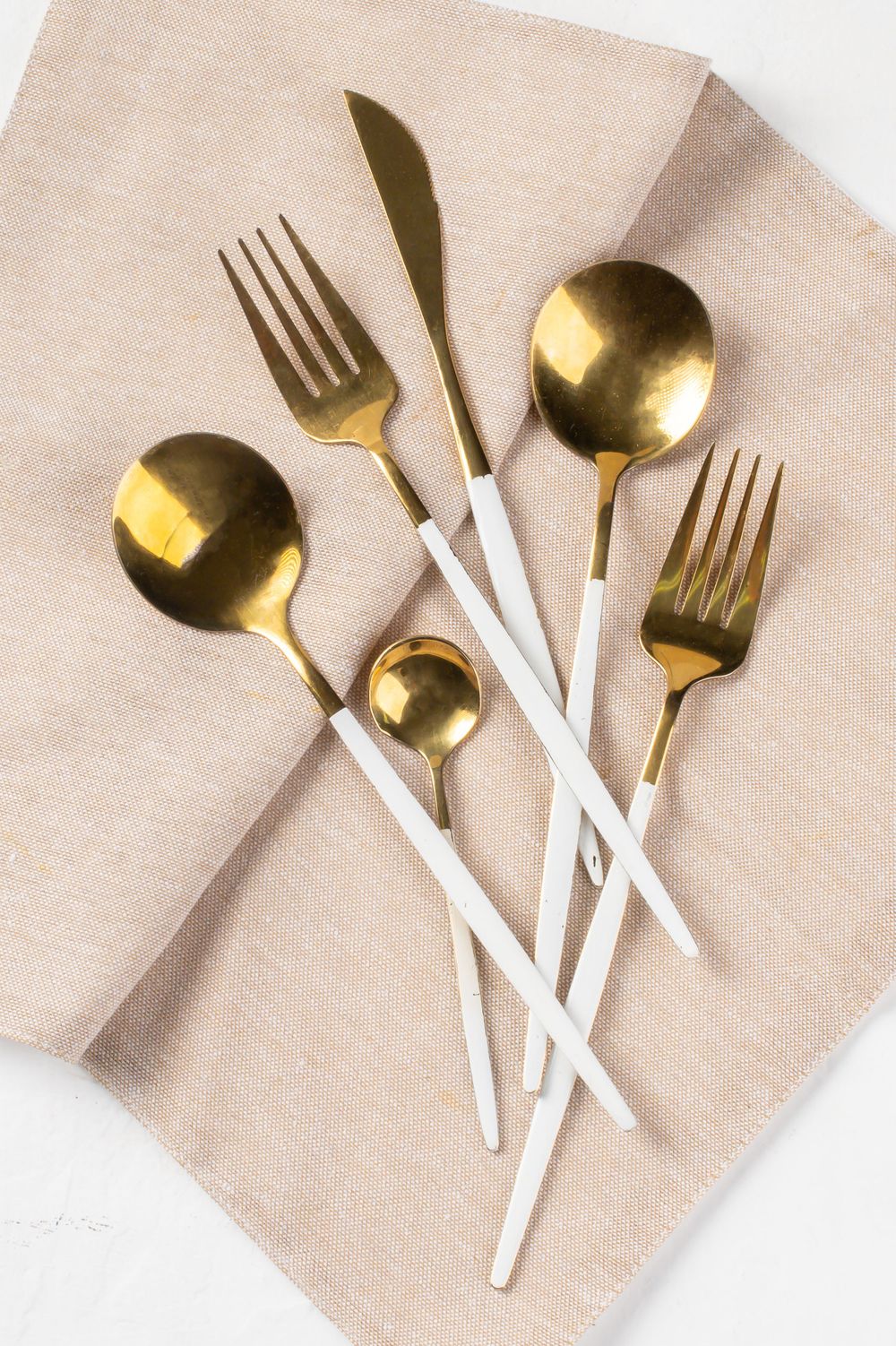Gold and white modern flatware set arranged on beige linen napkin.