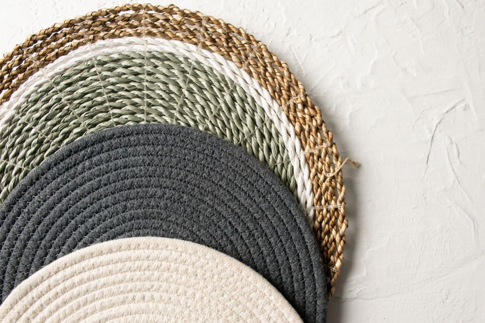 Stacked round woven placemats in natural, grey and white colors.