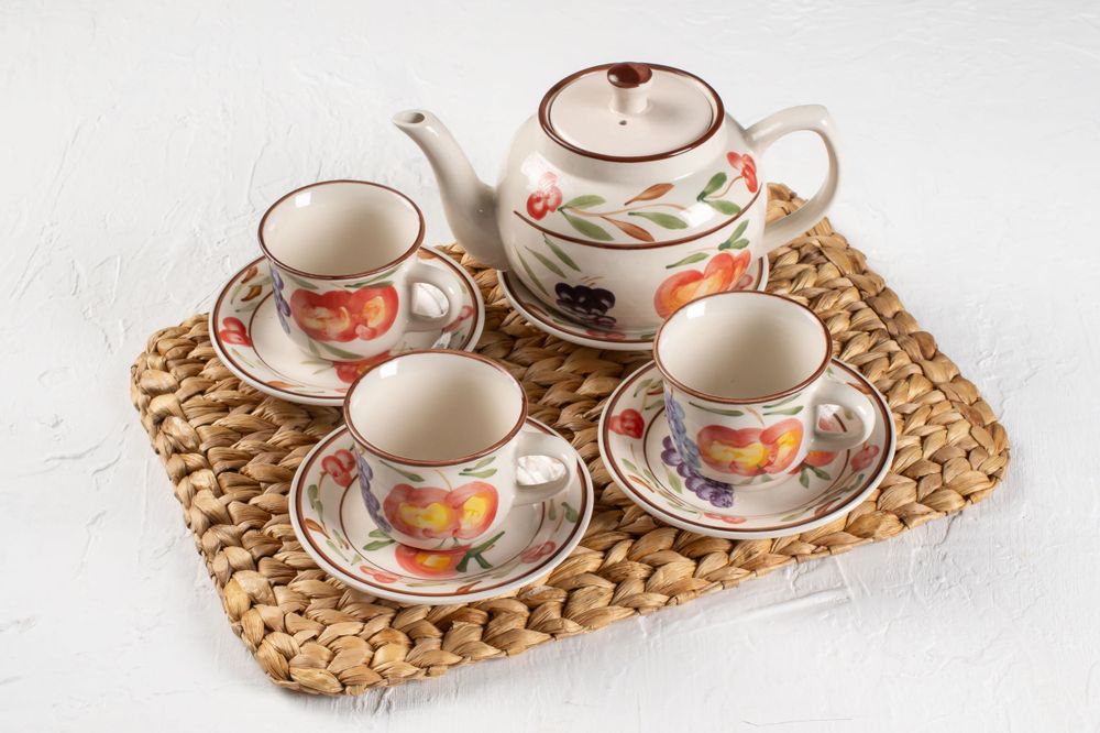 Vintage floral teapot set with cups on woven placemat.