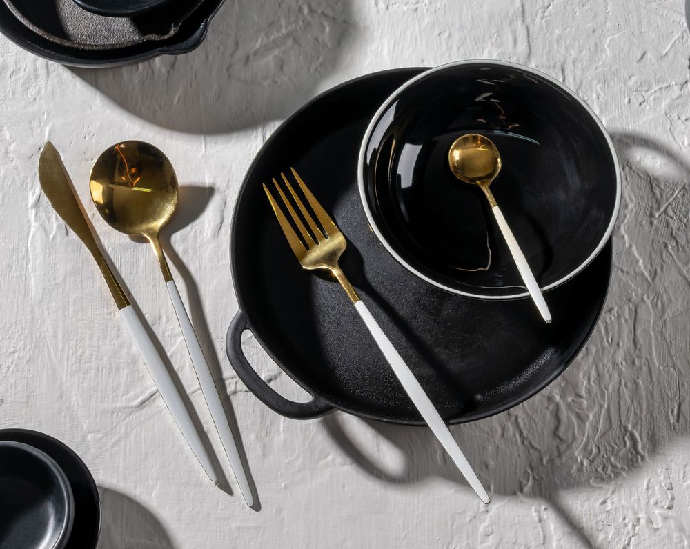 Elegant black plates and gold utensils arranged in a minimalist style against a white textured background.