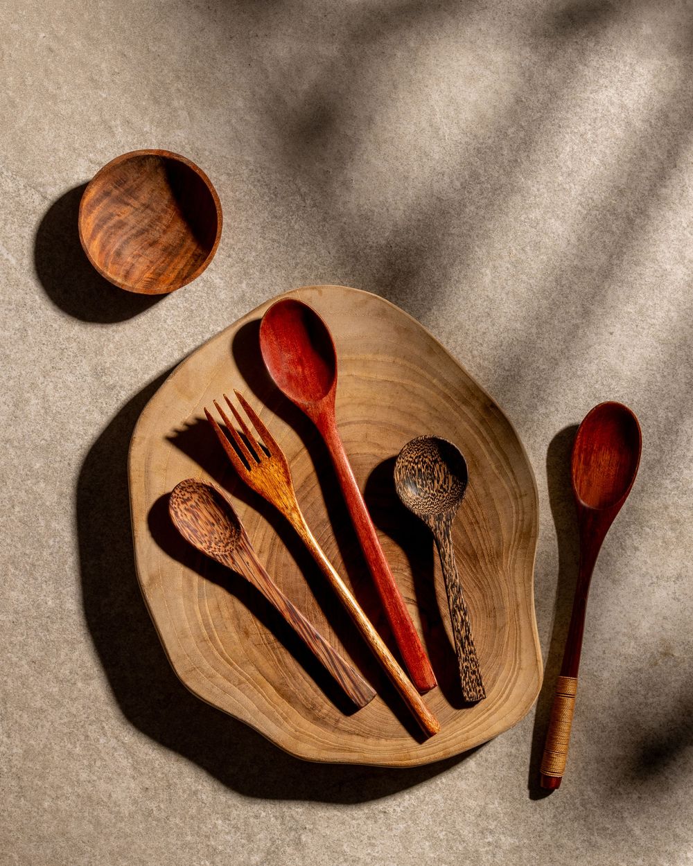 Artisanal wooden spoons and utensils arranged on a natural wood serving plate.