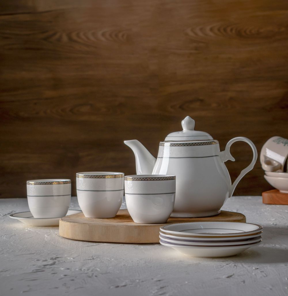 Modern white ceramic dinnerware and teapots displayed on a wooden surface.