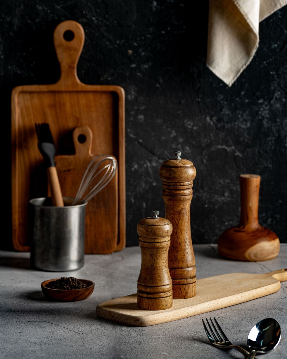 Rustic wooden kitchen accessories including cutting boards, pepper mills and utensils against a dark background.