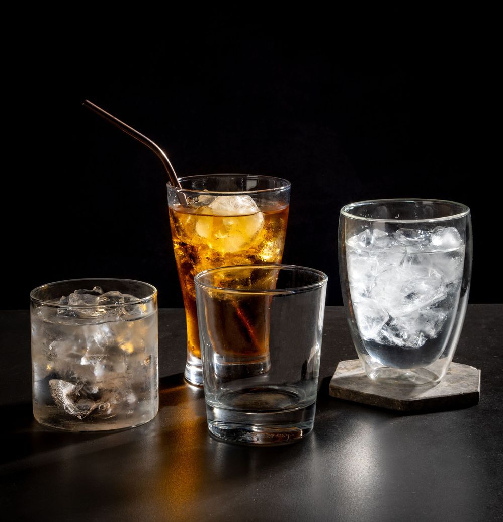 Elegant cocktail glasses with ice cubes and amber liquid on dark surface.