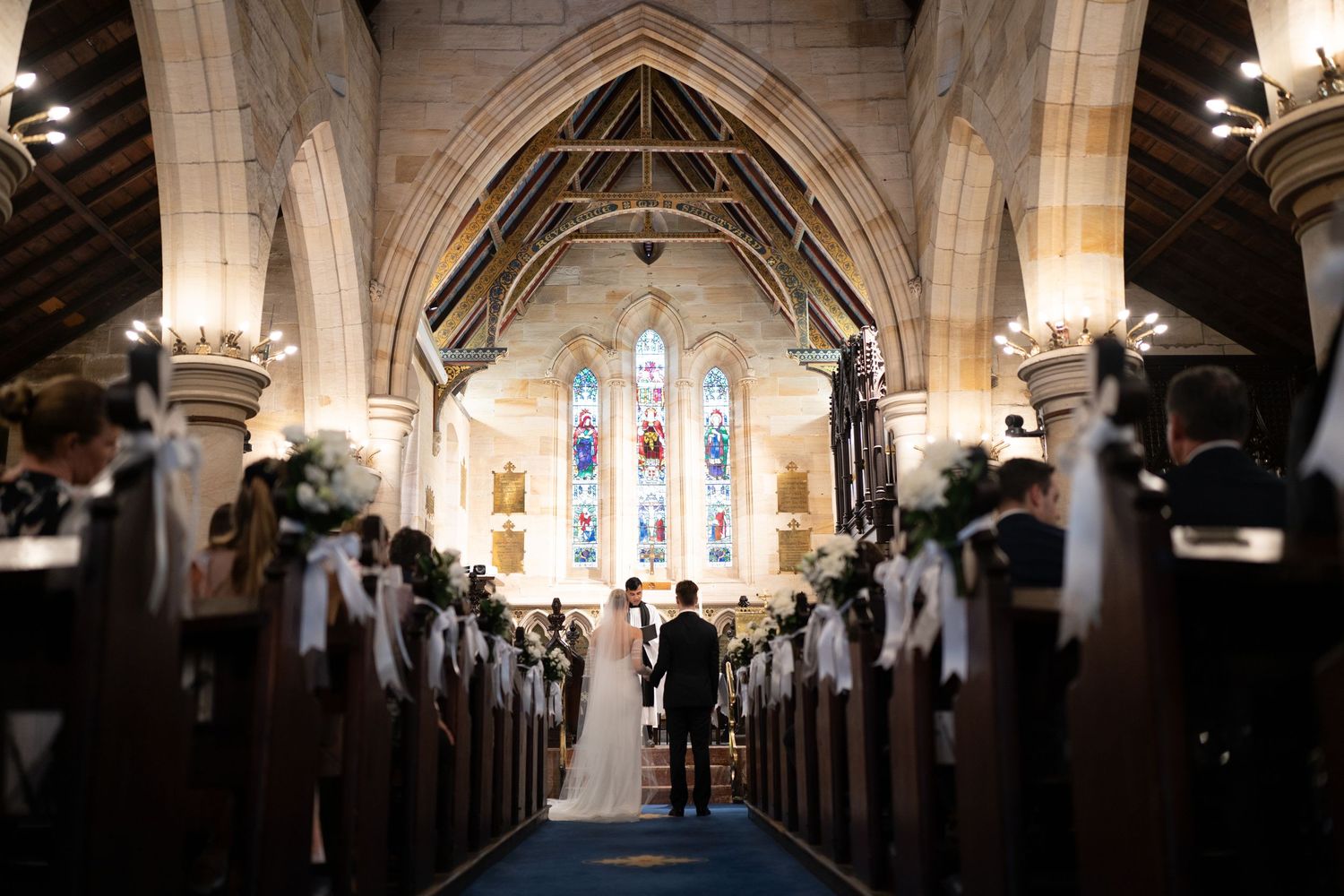 Wide angle view of wedding ceremony in traditional church with stained glass windows.