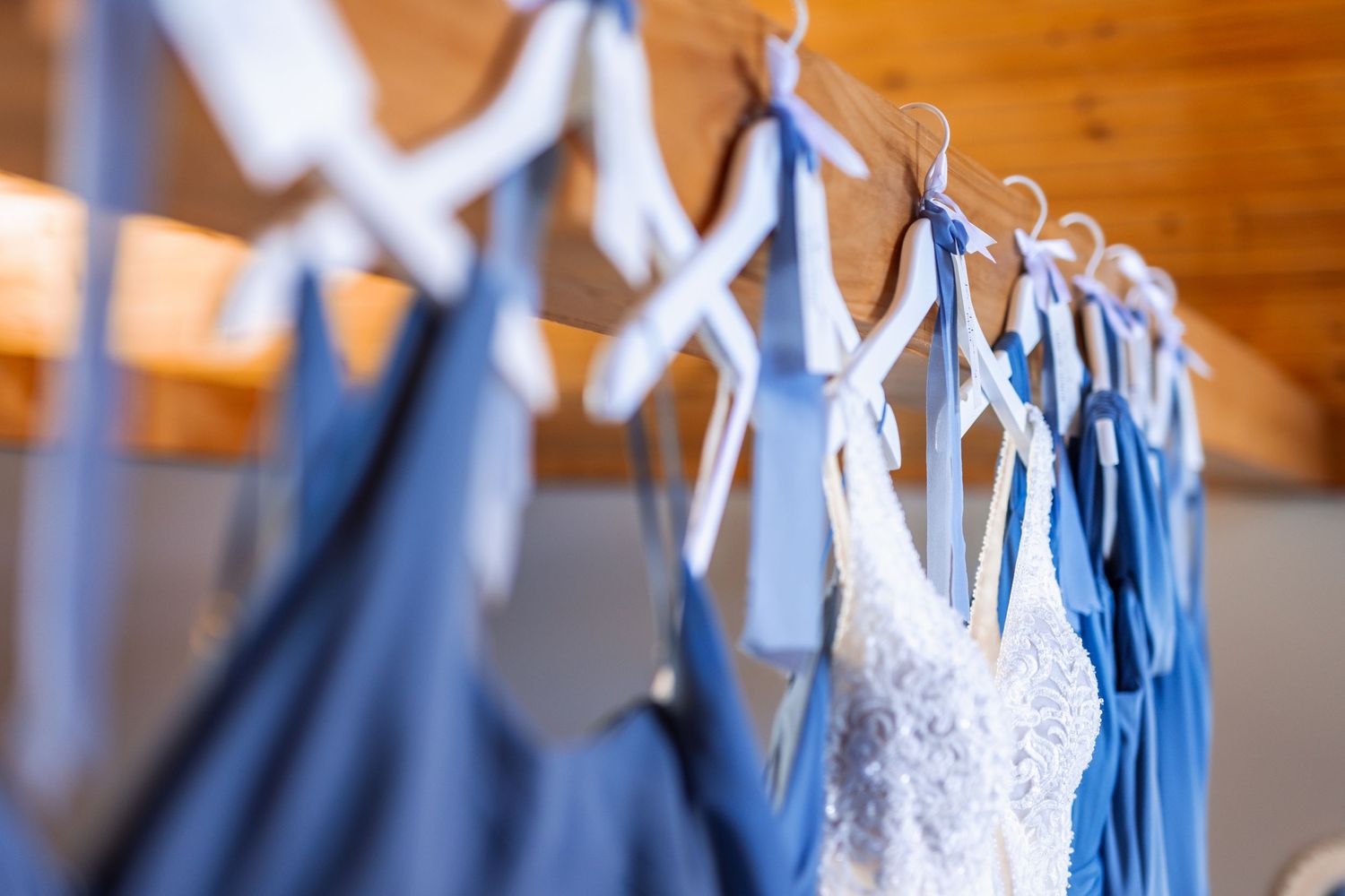Row of blue and white bridesmaid dresses hanging on wooden hangers.