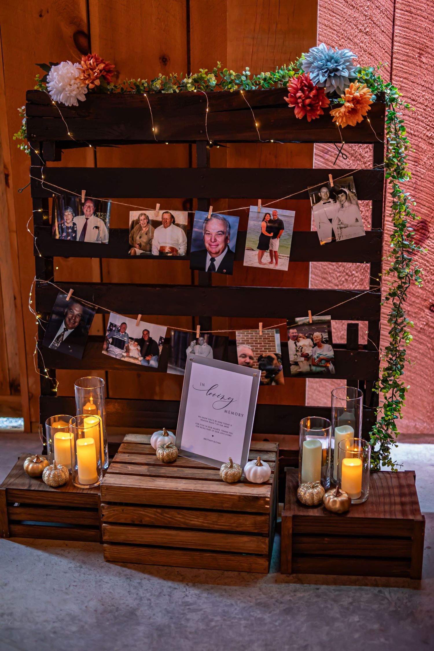 Rustic wooden pallet display with photos, flowers, and glowing candles creating an elegant memory wall.