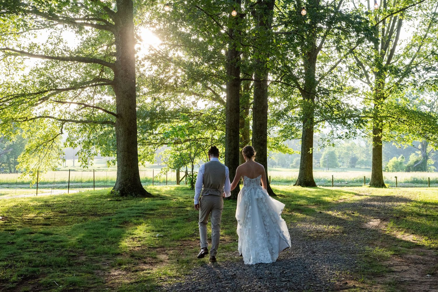 Wedding photo in a sunlit field with a flowing veil caught in the breeze against autumn trees at sunset.