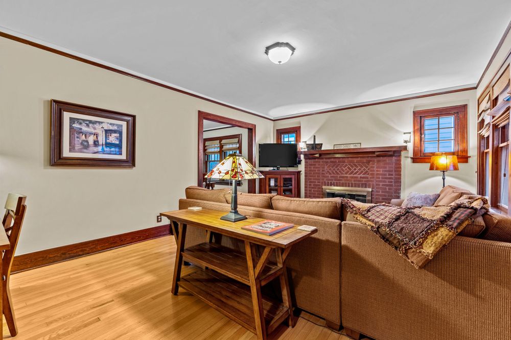 Cozy living room with brick fireplace, wicker sectional sofa, hardwood floors, and warm wood trim accents.
