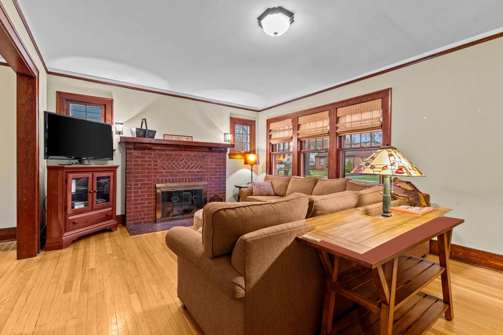 Traditional living room featuring brick fireplace, brown sectional sofa, hardwood floors, and Tiffany-style lamp.