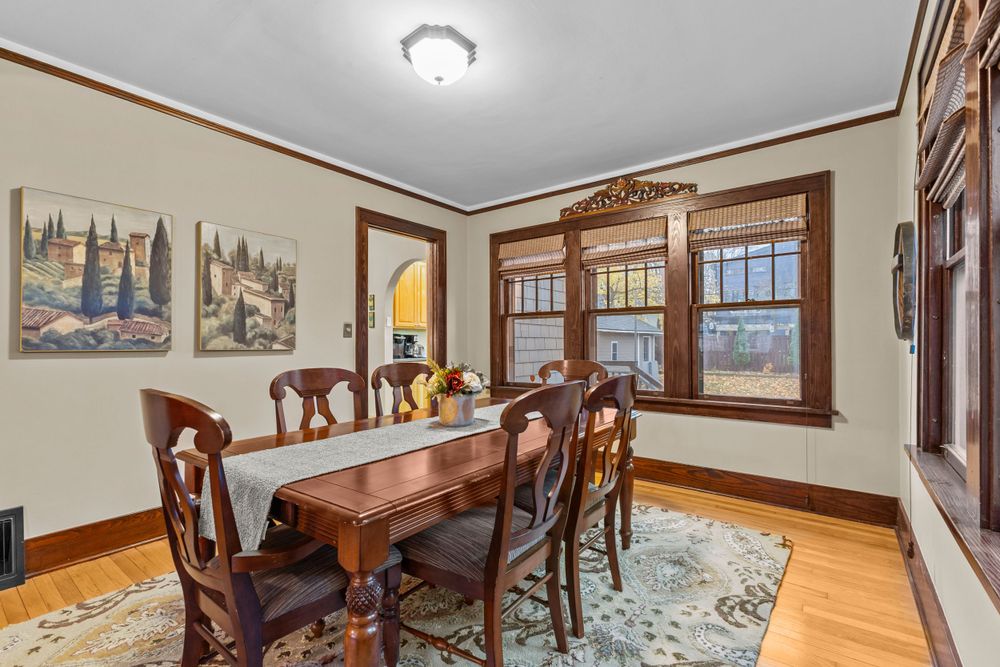 Formal dining room with dark wood table, six chairs, patterned area rug, and craftsman-style wood trim windows.