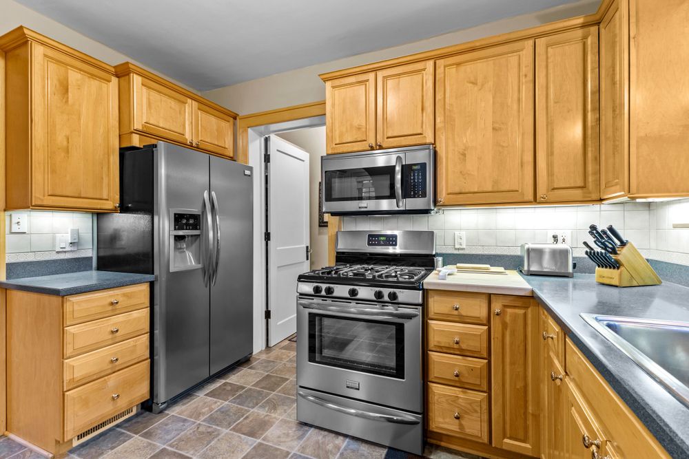 Modern kitchen featuring oak cabinetry, stainless steel refrigerator, gas range, microwave, and dark countertops.