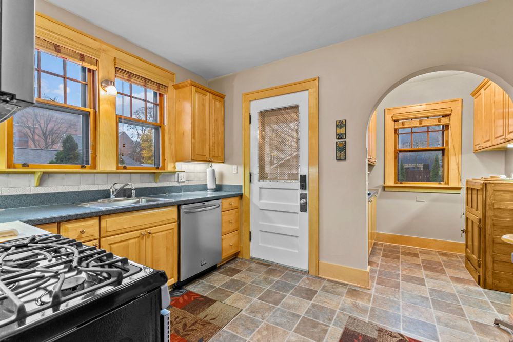 Bright kitchen with oak cabinets, stainless appliances, tile flooring, and charming arched doorway detail.