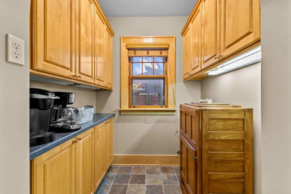 Narrow butler pantry with oak upper and lower cabinets, dark countertops, and slate tile flooring.