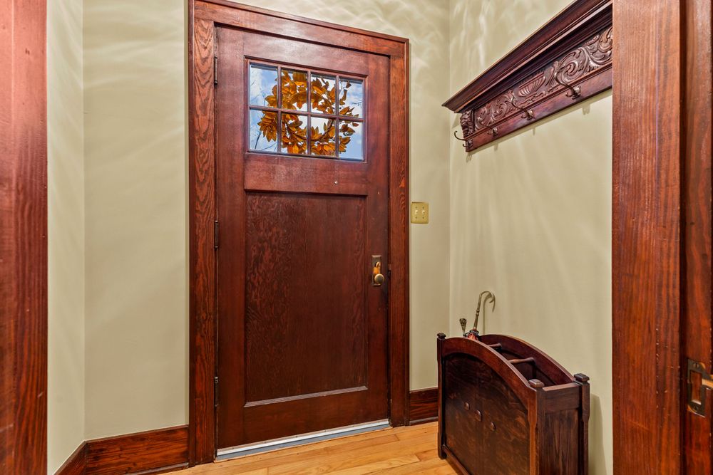 Classic entryway with rich wood front door, decorative wreath, ornate coat rack, and hardwood floors.