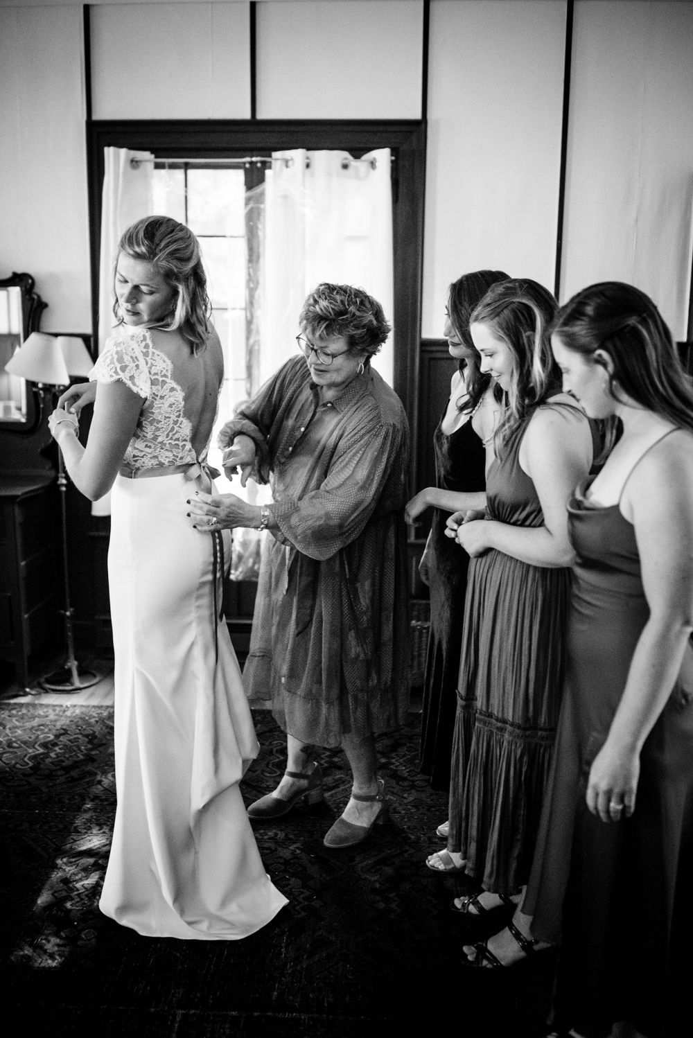 Black and white photo of bride being helped into wedding dress by bridesmaids.
