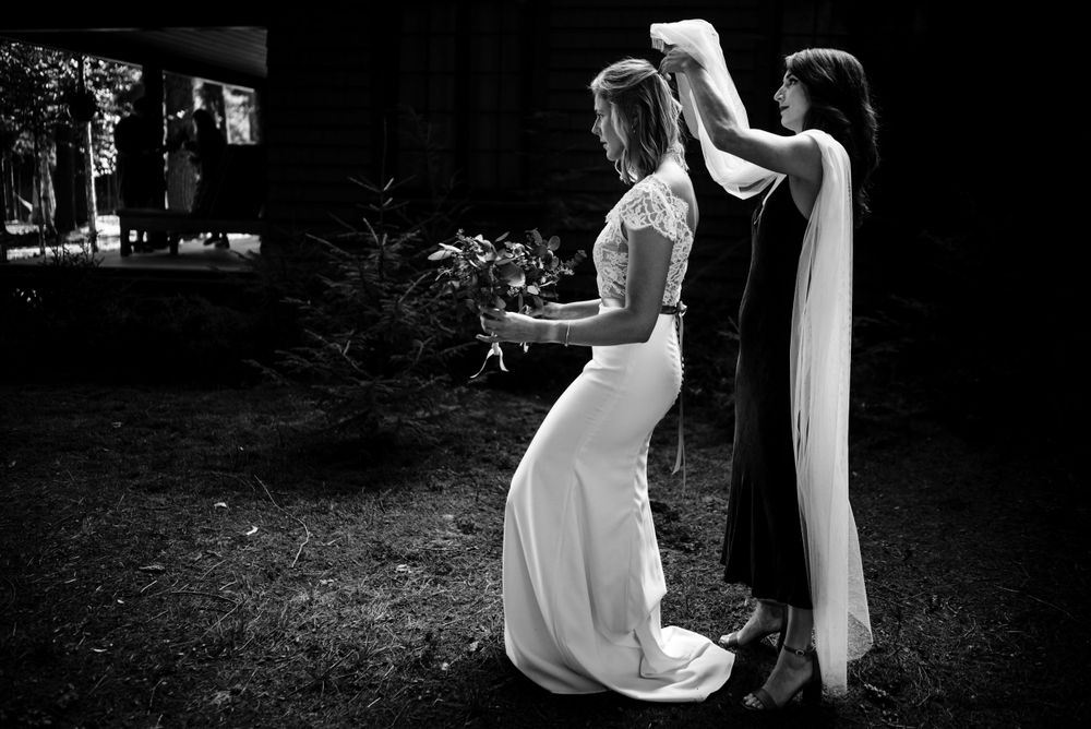 Black and white photo of bridesmaid adjusting brides veil outdoors before wedding.