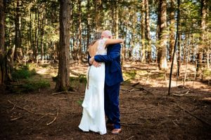 Bride and groom share tender first look embrace in sunlit forest setting.