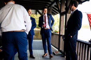 Groomsmen in navy blue suits laughing and socializing on a covered wooden porch before a wedding ceremony.