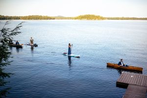 Wedding guests enjoying paddle boarding and canoeing on a calm lake surrounded by lush green trees.