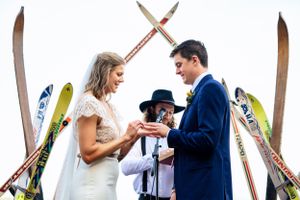 Bride and groom exchange rings during unique outdoor wedding ceremony with vintage skis as backdrop.
