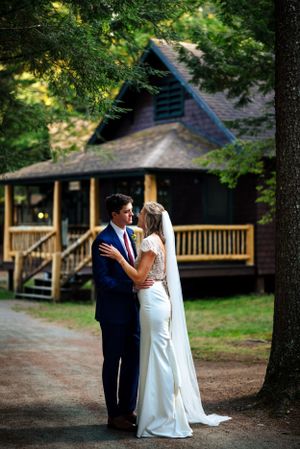 Bride and groom share a tender moment on a wooded path in front of a rustic cabin.