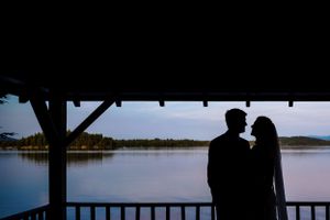Silhouette of bride and groom sharing an intimate moment on a porch overlooking a serene lake.