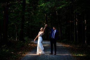 Bride and groom dancing on a forest path in dappled sunlight during their outdoor wedding.