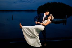 Groom dipping bride in a romantic kiss on a lakeside dock at twilight.