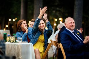 Excited wedding guest raises hands in celebration at an outdoor evening reception.