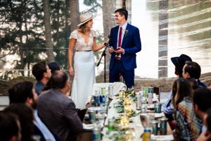 Bride and groom share a microphone while giving speeches at an outdoor wedding reception.