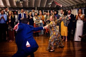 Wedding guest in floral dress spins joyfully on dance floor with guest in blue suit.