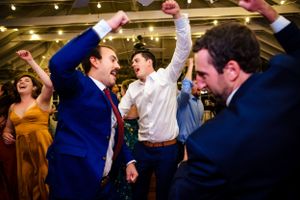 Joyful groomsmen in blue suits celebrate with raised fists on the wedding reception dance floor.