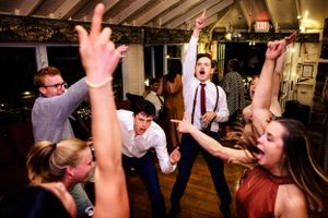 Energetic wedding guests dance with arms raised in celebration at lively reception party.