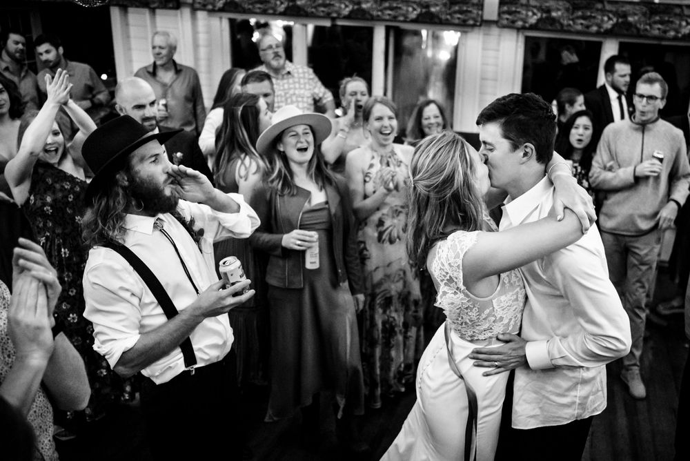 Bride and groom share a heartfelt kiss on the dance floor surrounded by celebrating wedding guests.