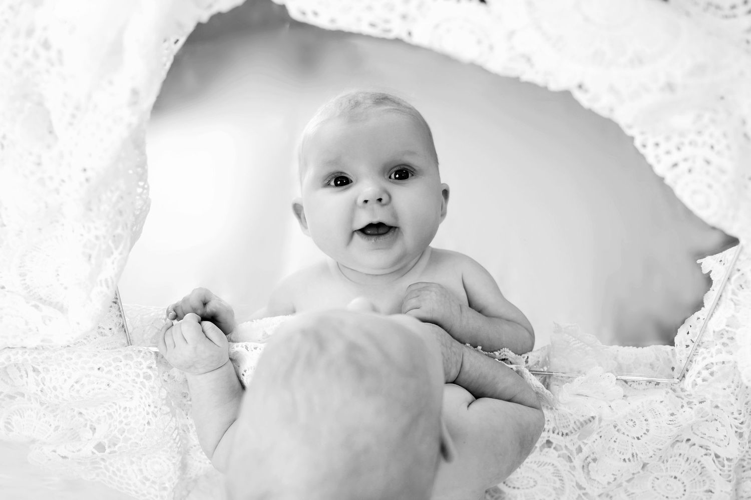 Black and white photo of an infant peeking through white lace fabric.