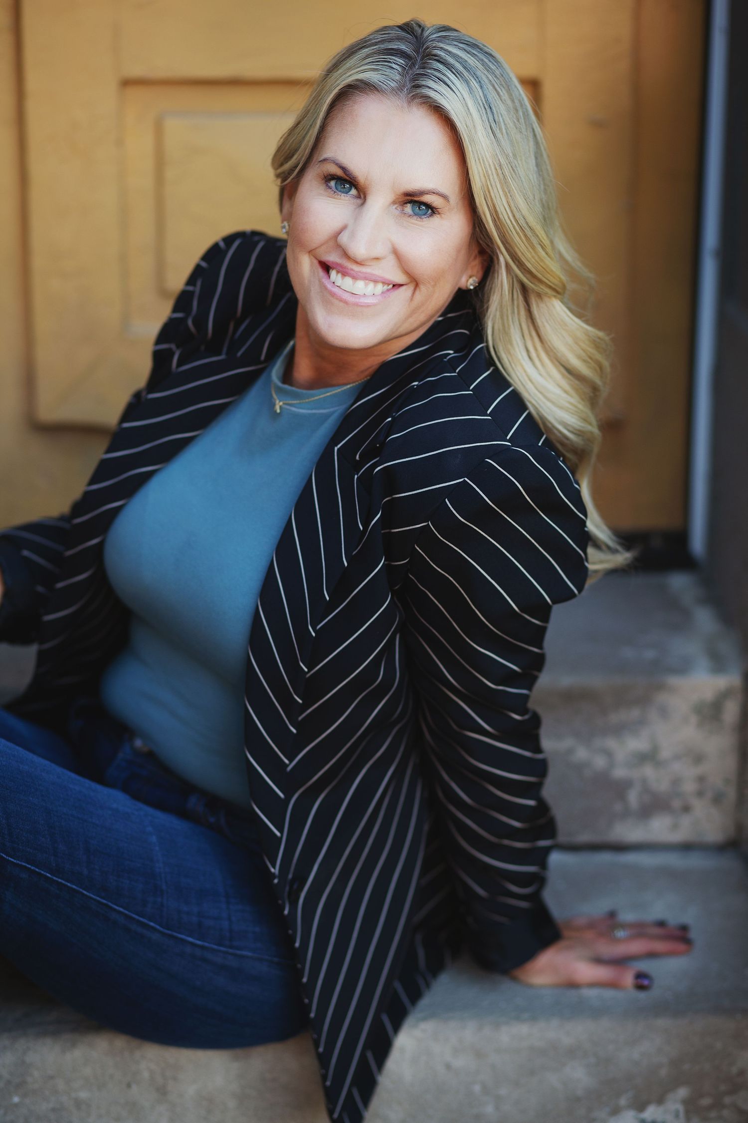 headshot of smiling blond woman sitting on steps with black and white striped jacket downtown louisville