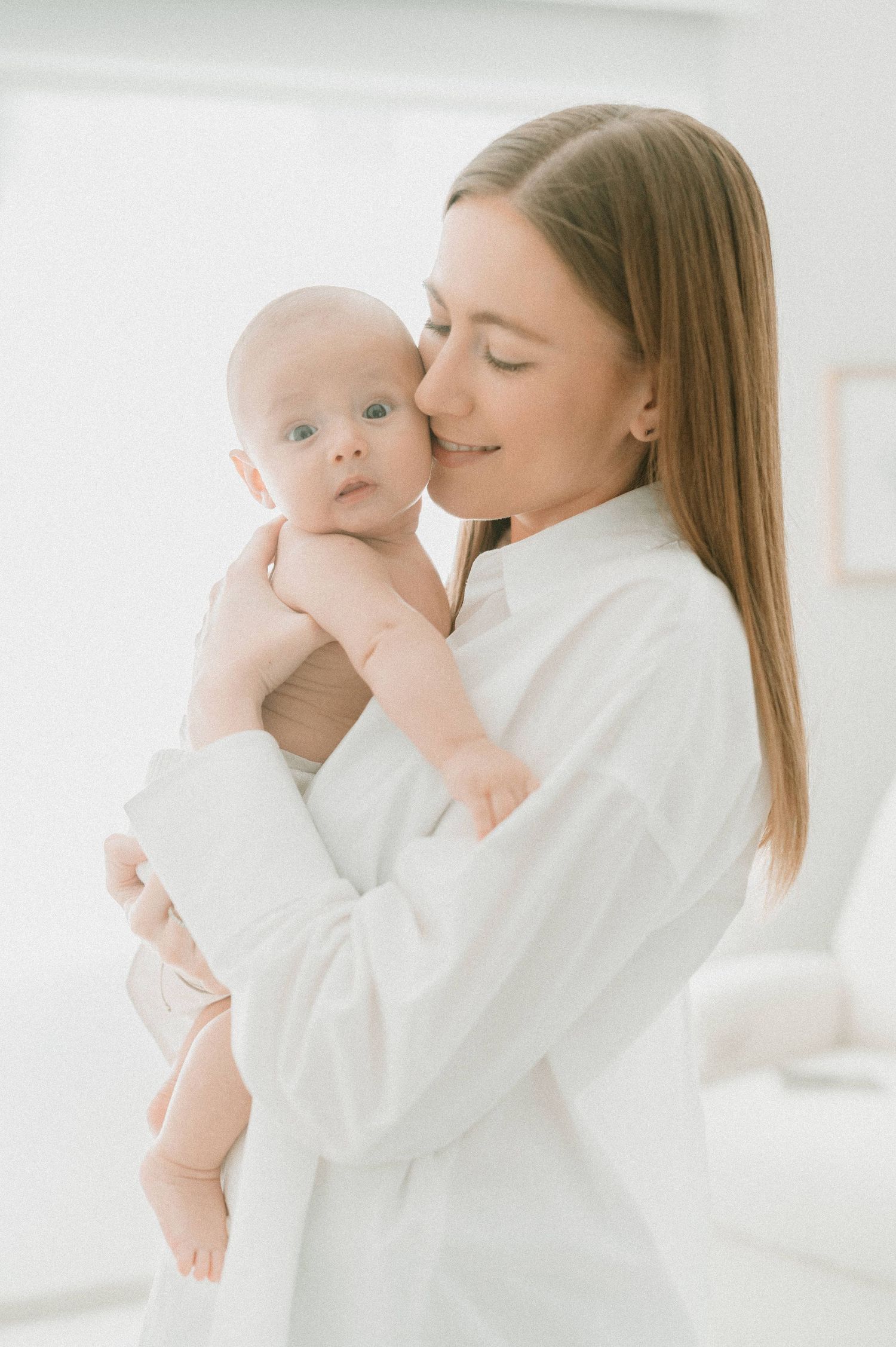 Tender family moment with baby in bright white minimalist setting.