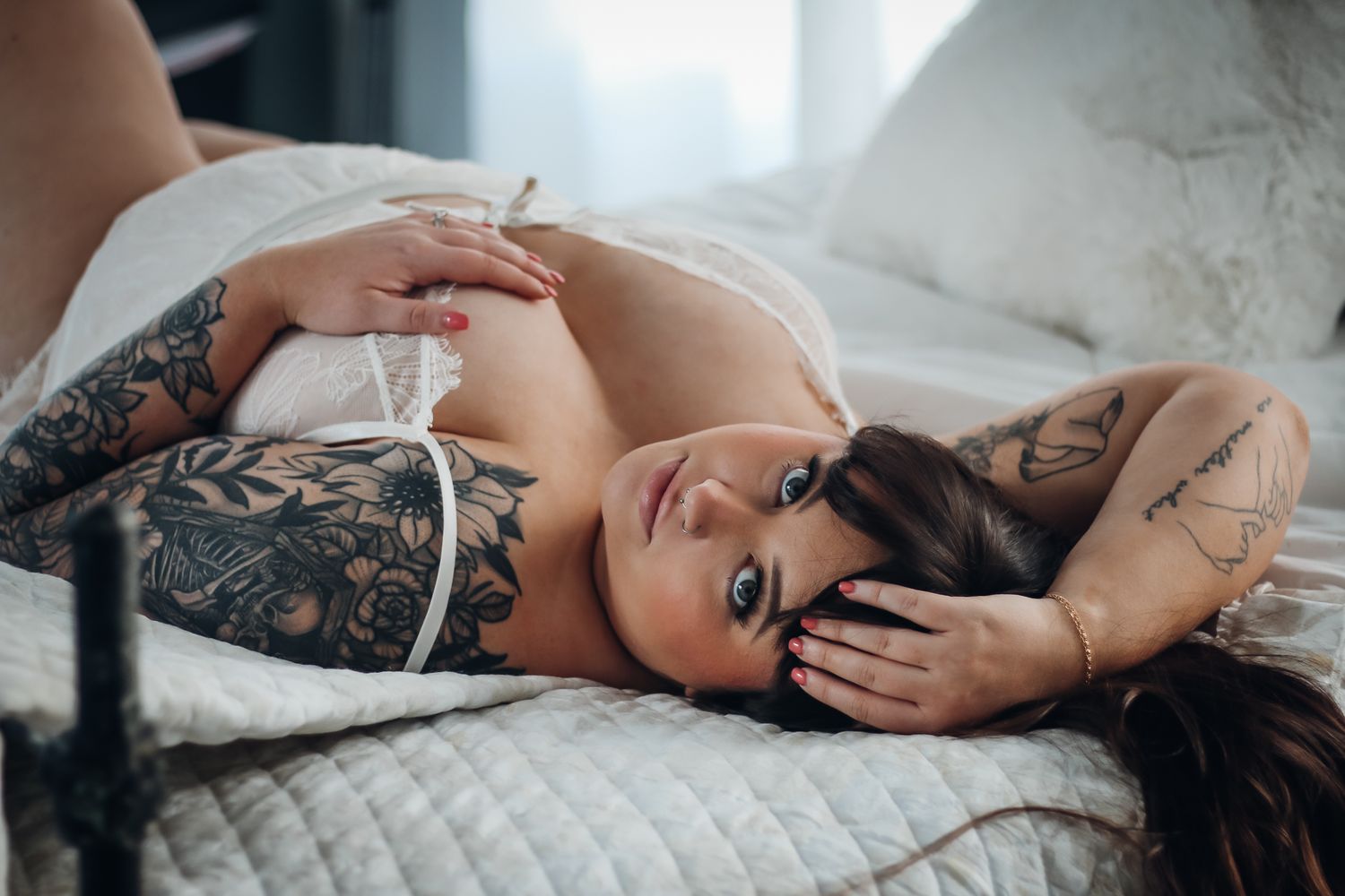 Woman in black lace lingerie poses sensually on white bedding. Boudoir photography