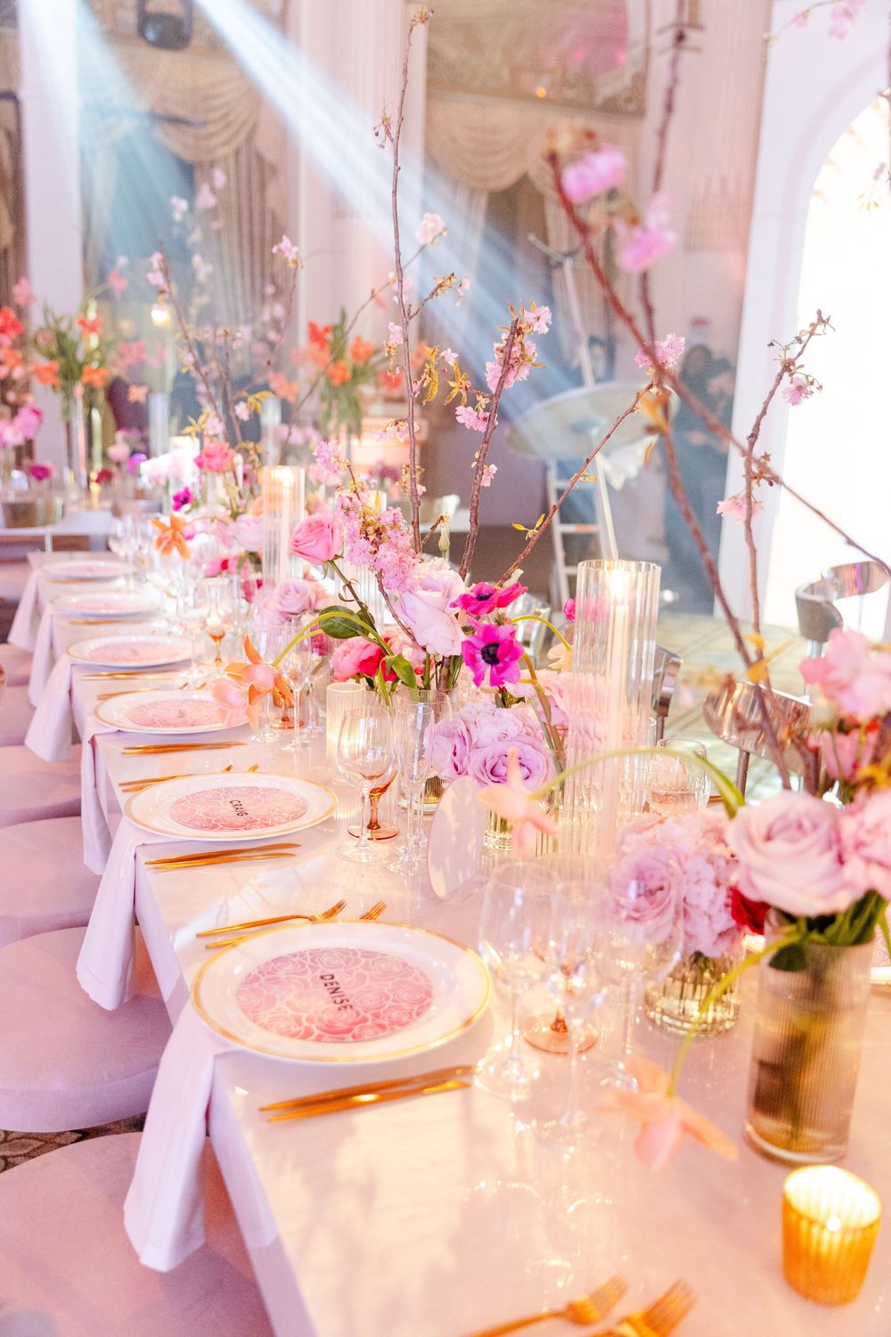 Elegant wedding reception table settings with pink floral centerpieces, white linens, and warm candlelight create a romantic atmosphere.