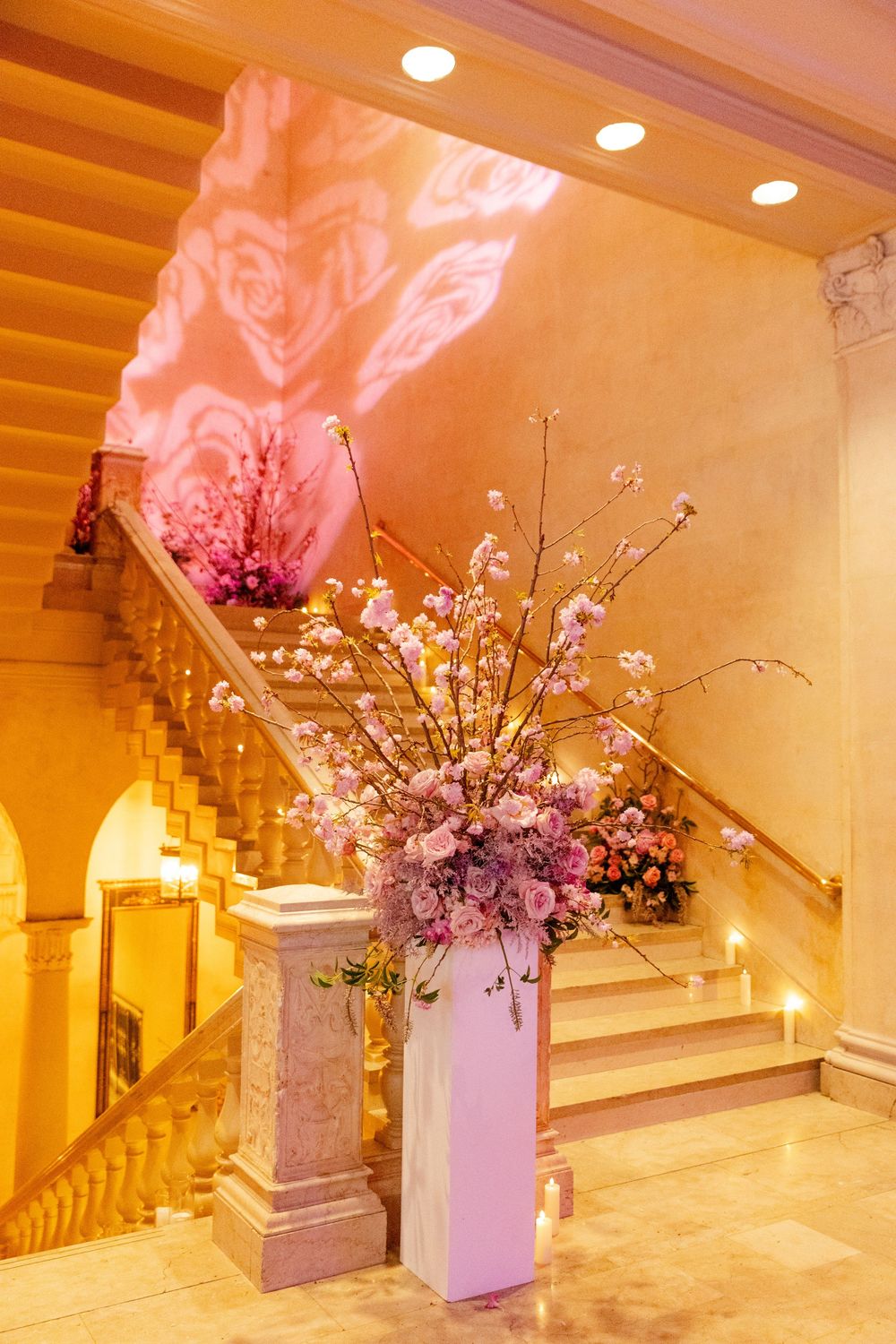 Elegant grand entrance hall with warm lighting and ornate floral arrangements featuring cherry blossoms and dramatic staircases.