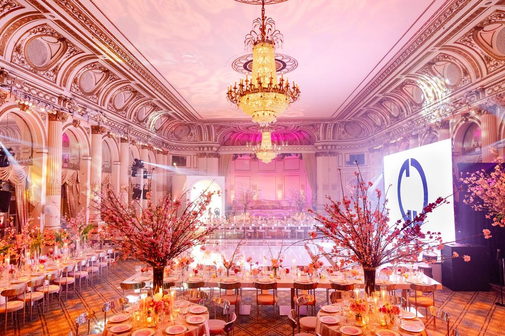 Luxurious ballroom with pink lighting, crystal chandelier and cherry blossom centerpieces.